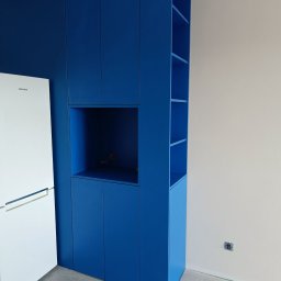 HiWall - Meble na Wymiar Wrocław - Niebieska zabudowa meblowa w kuchni z otwartymi półkami i miejscem na lodówkę, widoczne gniazdko elektryczne w ścianie.