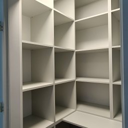 HiWall - Meble na Wymiar Wrocław - Wnętrze białej, pustej garderoby z półkami, widok z dołu na narożną konstrukcję z podziałem na liczne kwadratowe i prostokątne przegródki.
