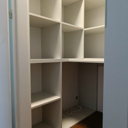 HiWall - Meble na Wymiar Wrocław - Wnętrze białej, narożnej garderoby z półkami, widoczne zawiasy drzwi i kabel zasilający w dolnej części.