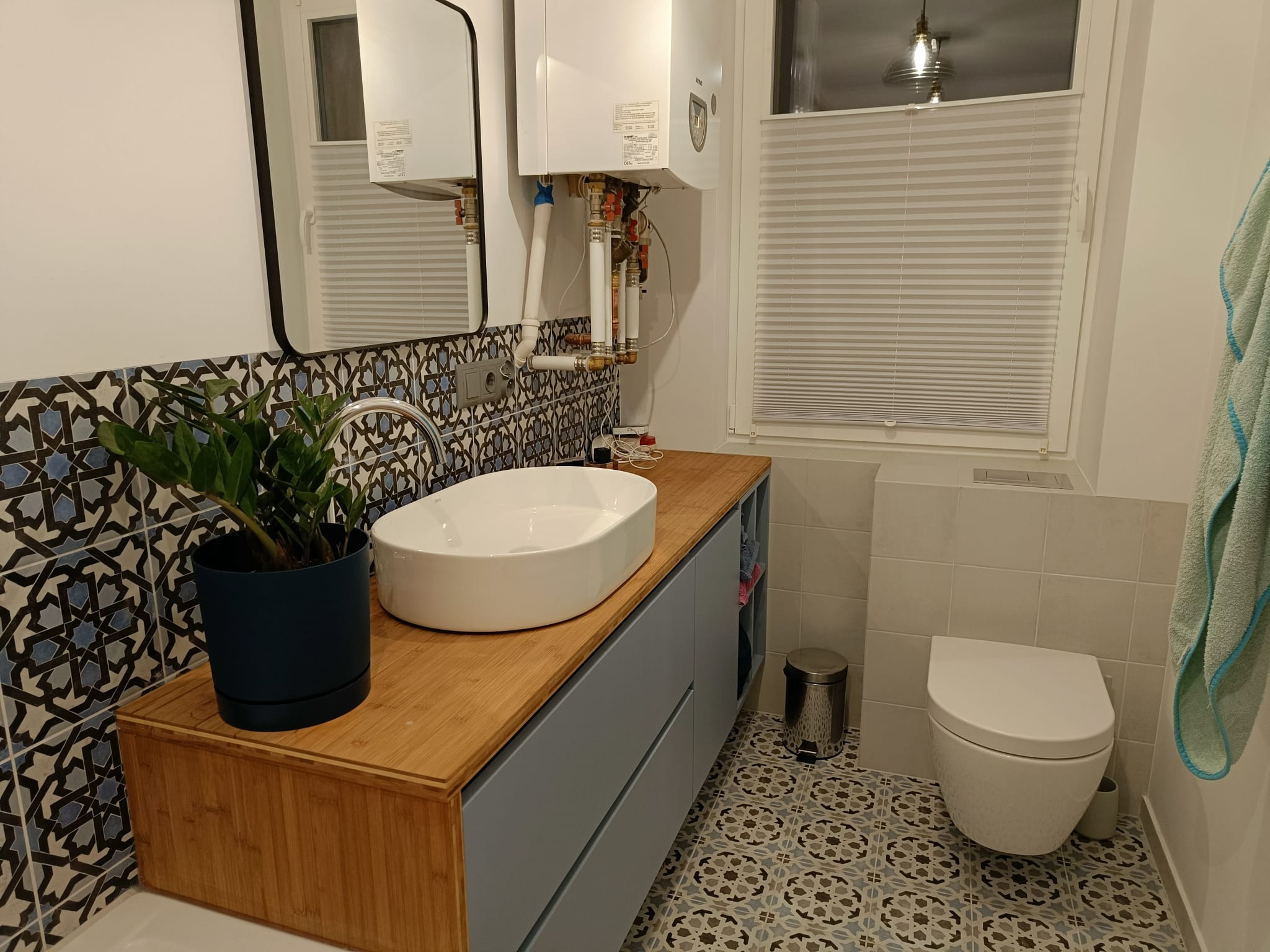 Nowoczesna łazienka z drewnianym blatem, umywalką nablatową, wzorzystymi płytkami i wiszącym piecem gazowym nad umywalką.