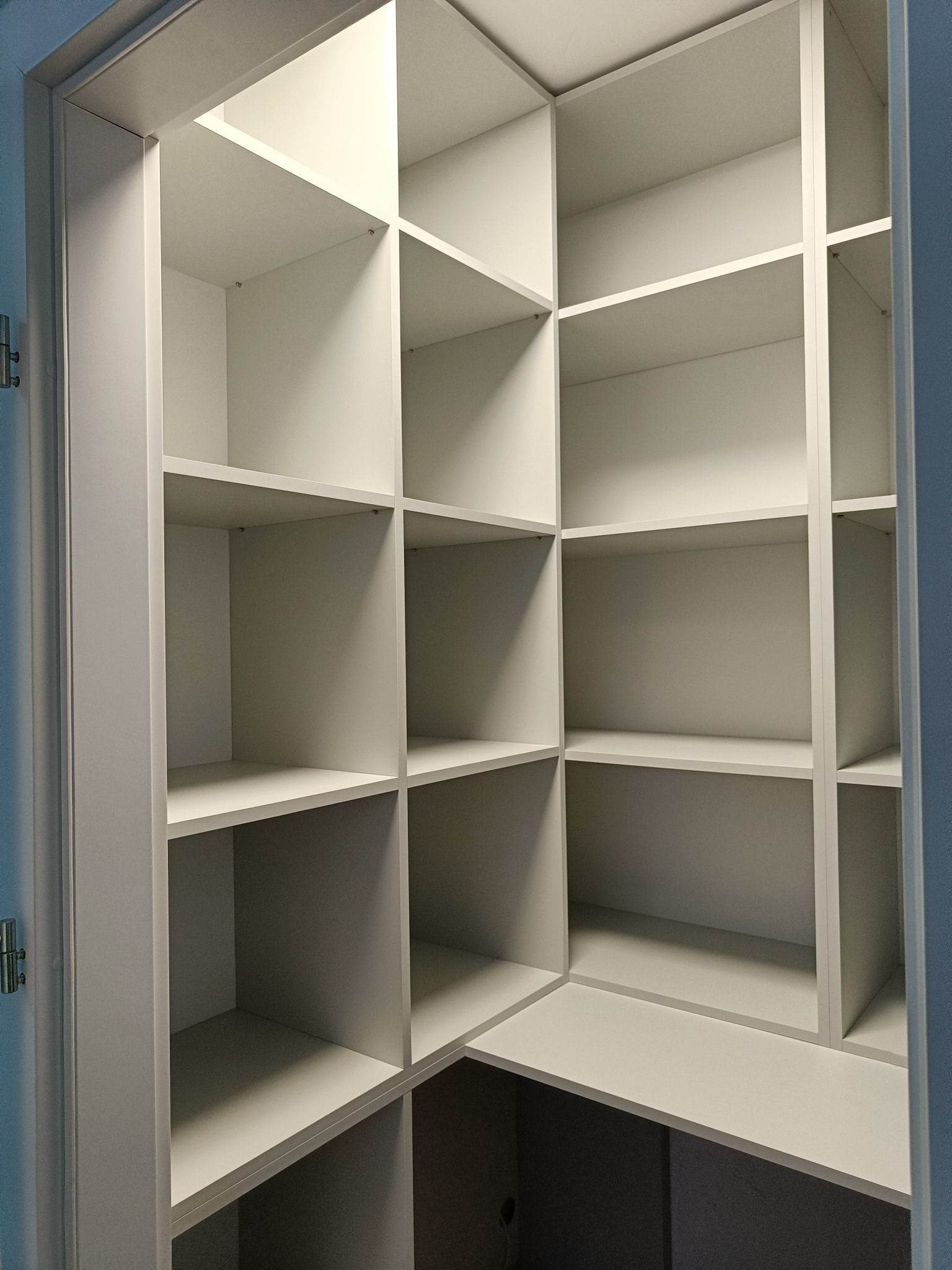 Wnętrze białej, pustej garderoby z półkami, widok z dołu na narożną konstrukcję z podziałem na liczne kwadratowe i prostokątne przegródki.