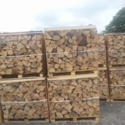 Ułożone na paletach, zabezpieczone siatką i taśmą pakiety z pociętymi kawałkami drewna, przygotowane do transportu i składowania.