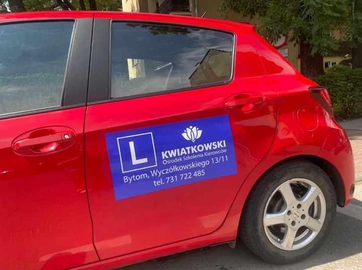Czerwony samochód z niebieską naklejką 'L' i logo szkoły nauki jazdy 'KWIATKOWSKI' z adresem i numerem telefonu w Bytomiu.
