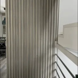 Dekoracyjna ścianka działowa z drewnianych lameli w odcieniach szarości, oddzielająca przestrzeń, widoczna z perspektywy schodów z metalową balustradą.