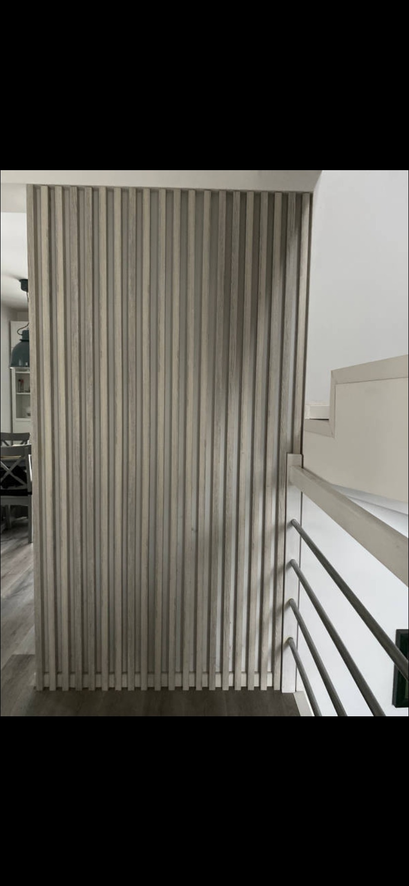 Dekoracyjna ścianka działowa z drewnianych lameli w odcieniach szarości, oddzielająca przestrzeń, widoczna z perspektywy schodów z metalową balustradą.