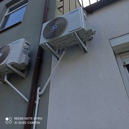 Optima Klima - Dwa klimatyzatory marki Kaisai zamontowane na elewacji budynku, widoczne rury odprowadzające skropliny.