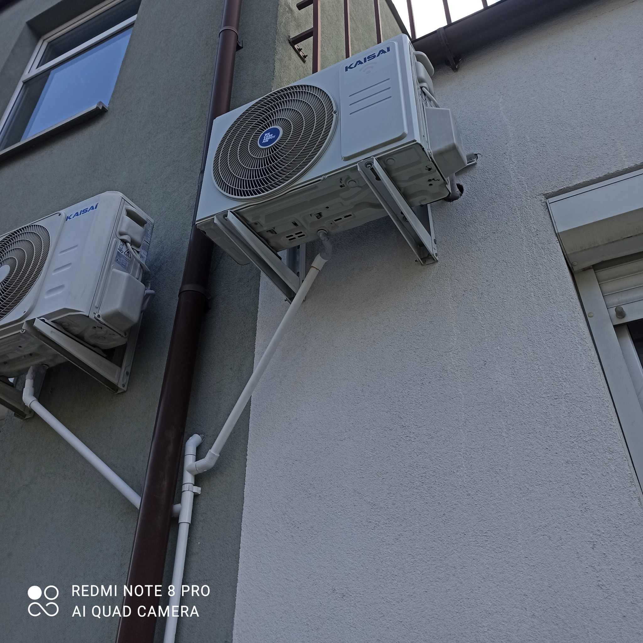 Dwa klimatyzatory marki Kaisai zamontowane na elewacji budynku, widoczne rury odprowadzające skropliny.