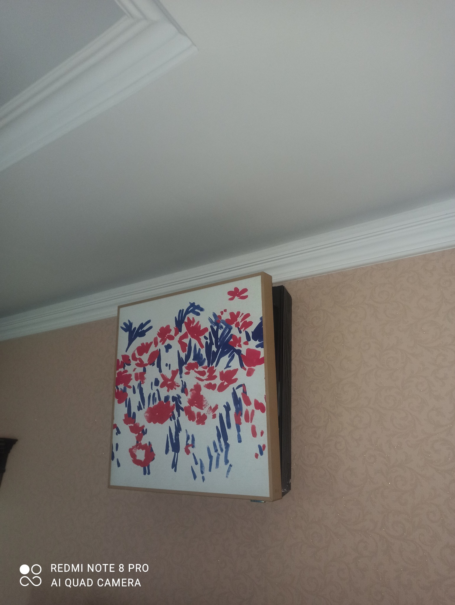 Klimatyzator ścienny z niestandardową obudową ozdobioną motywem kwiatowym w czerwieni i granacie, zamontowany w pokoju z tapetą w delikatne wzory.