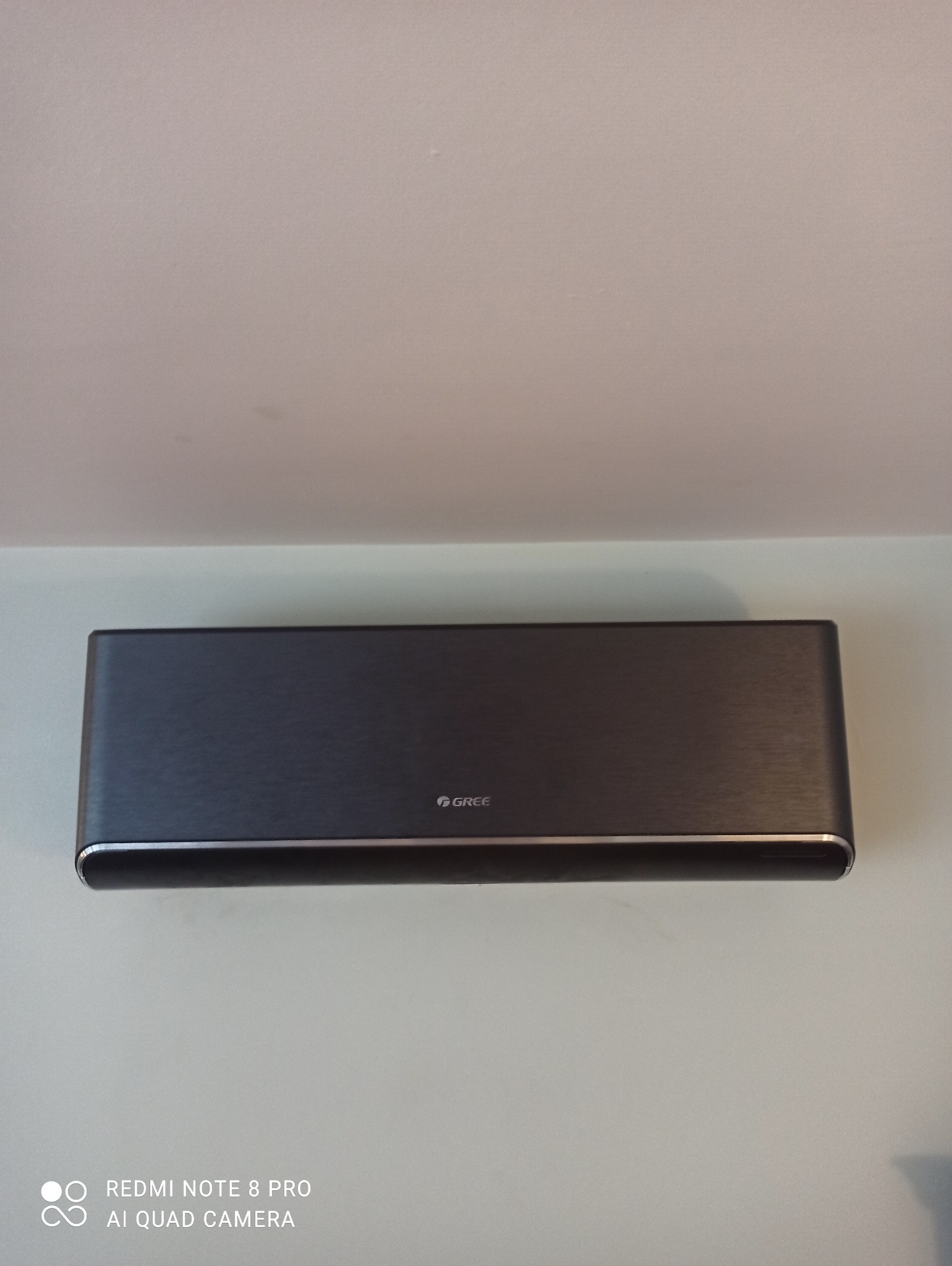 Szary klimatyzator marki Gree zamontowany na jasnej ścianie, widok z przodu, z widocznym logo.