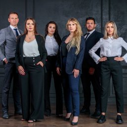 Tutenhoman Monika Homan - Profesjonalny portret grupowy sześciu osób w formalnych strojach na tle ciemnej ściany z panelami i drewnianej podłogi.