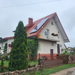 NASZA ENERGETYKA SPÓŁKA Z OGRANICZONĄ ODPOWIEDZIALNOŚCIĄ - Dom jednorodzinny z czerwonym dachem i panelami słonecznymi na dachu, widok z poziomu gruntu w pochmurny dzień.