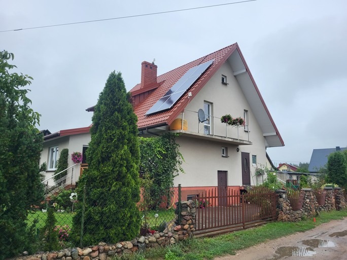 Dom jednorodzinny z czerwonym dachem i panelami słonecznymi na dachu, widok z poziomu gruntu w pochmurny dzień.