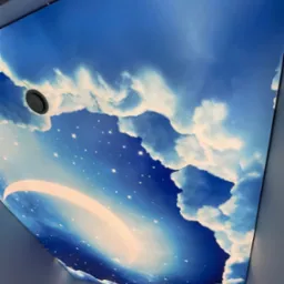 Nastrojowy sufit z motywem nieba: błękit, chmury i gwiazdy. Okrągły otw&oacute;r wentylacyjny wkomponowany w design, tworzy unikalny efekt wizualny w pomieszczeniu.