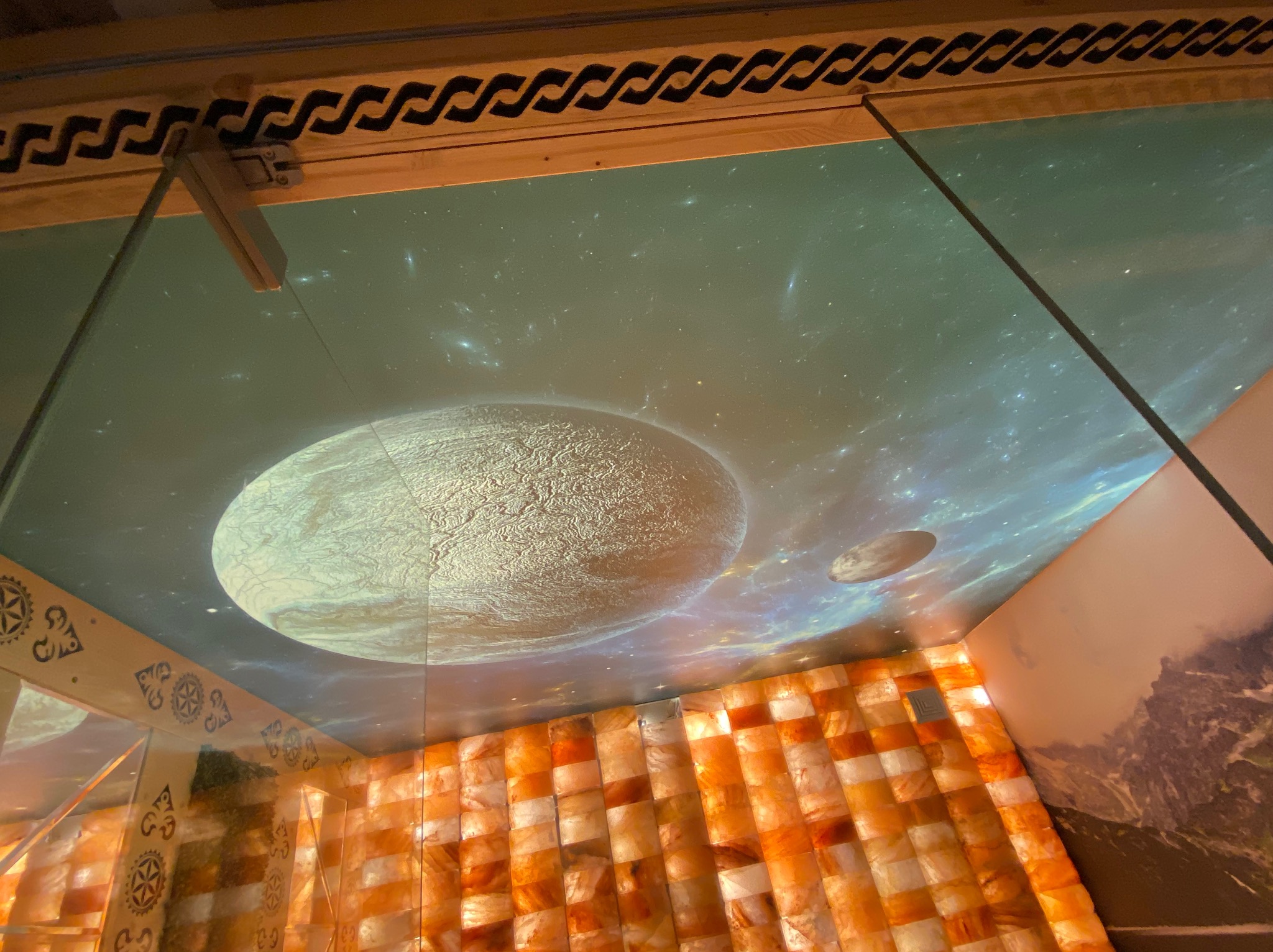 Sufit napinany z projekcją kosmosu i planet w pomieszczeniu wyłożonym cegłami solnymi, widoczne elementy dekoracyjne na ramie sufitu.
