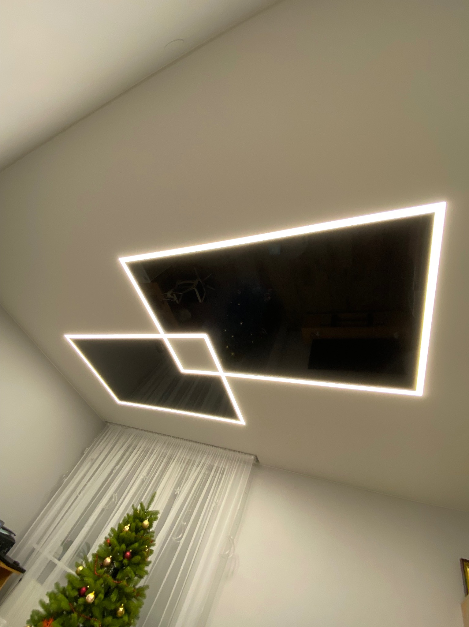 Nowoczesny, czarny sufit z oświetleniem LED w kształcie dwóch nachodzących na siebie kwadratów, widoczny fragment choinki i zasłony w tle.