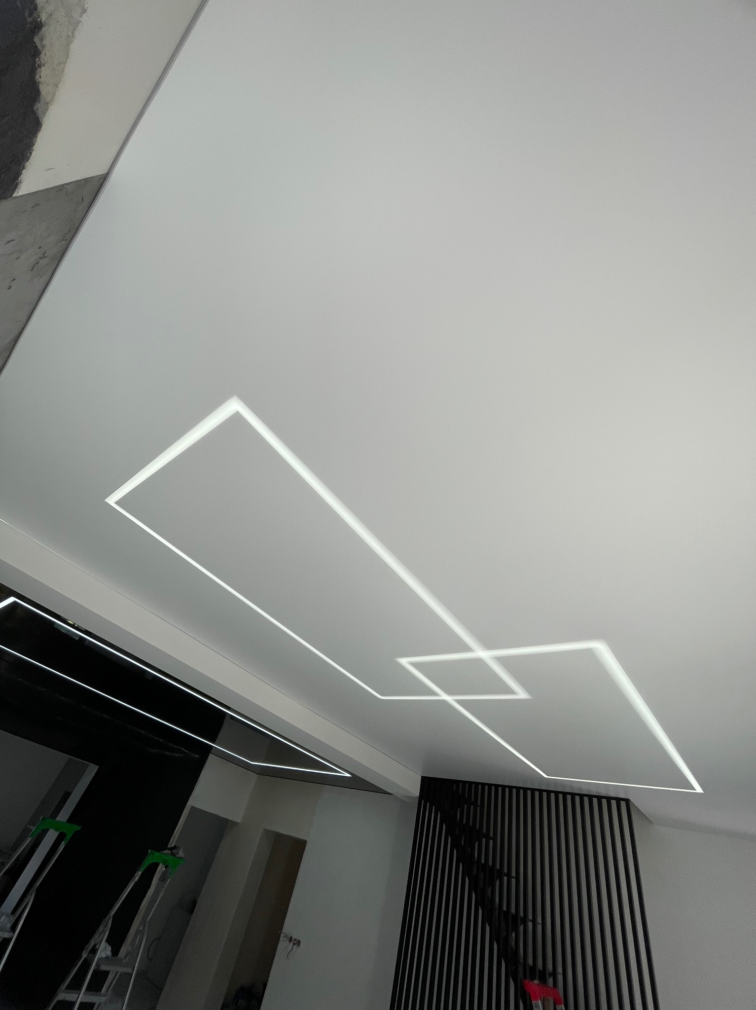 Biały sufit z napinanej membrany, podświetlony geometrycznym wzorem LED. Widok z dołu, fragment drabiny w rogu kadru.