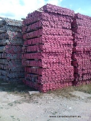 Sztaple budowlane ułożone w regularne stosy, część z nich pomalowana na różowo, widoczne na zewnątrz w słoneczny dzień.