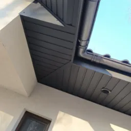 Nowoczesny, czarny system orynnowania zamontowany na podbitce dachu, widok z dołu na tle błękitnego nieba.