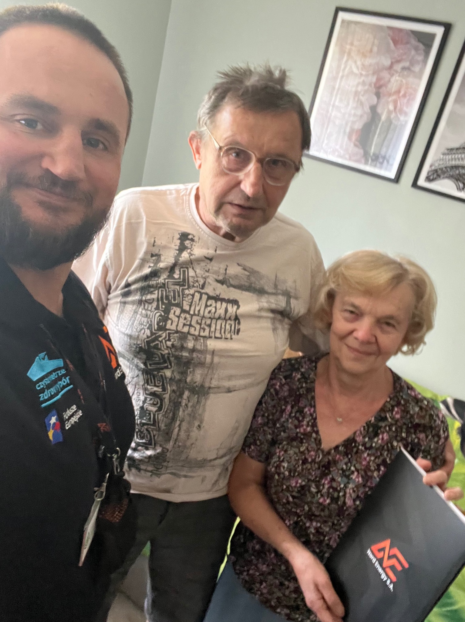 Selfie z klientami trzymającymi czarny folder Nord Energy S.A. z logo w mieszkaniu z obrazami na ścianie.