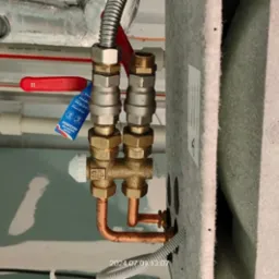 Przyłącze grzejnikowe z zaworami odcinającymi i termostatycznym, rurki miedziane, widoczna etykieta producenta zaworów, tło stanowią rury pod sufitem.