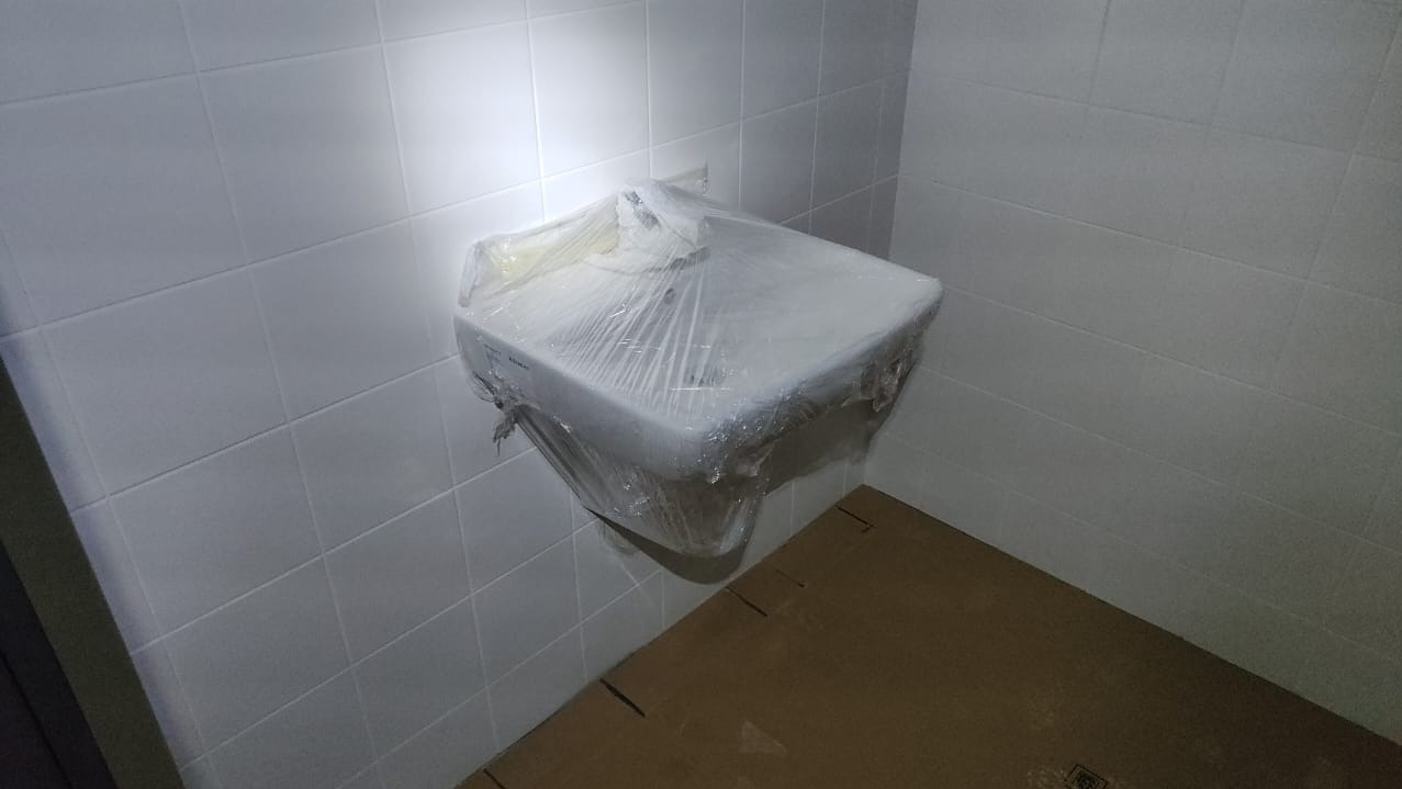 Nowa, biała umywalka, jeszcze zabezpieczona folią ochronną, zamontowana na białej, wykafelkowanej ścianie w łazience w Katowicach. Podłoga zabezpieczona kartonem podczas remontu.