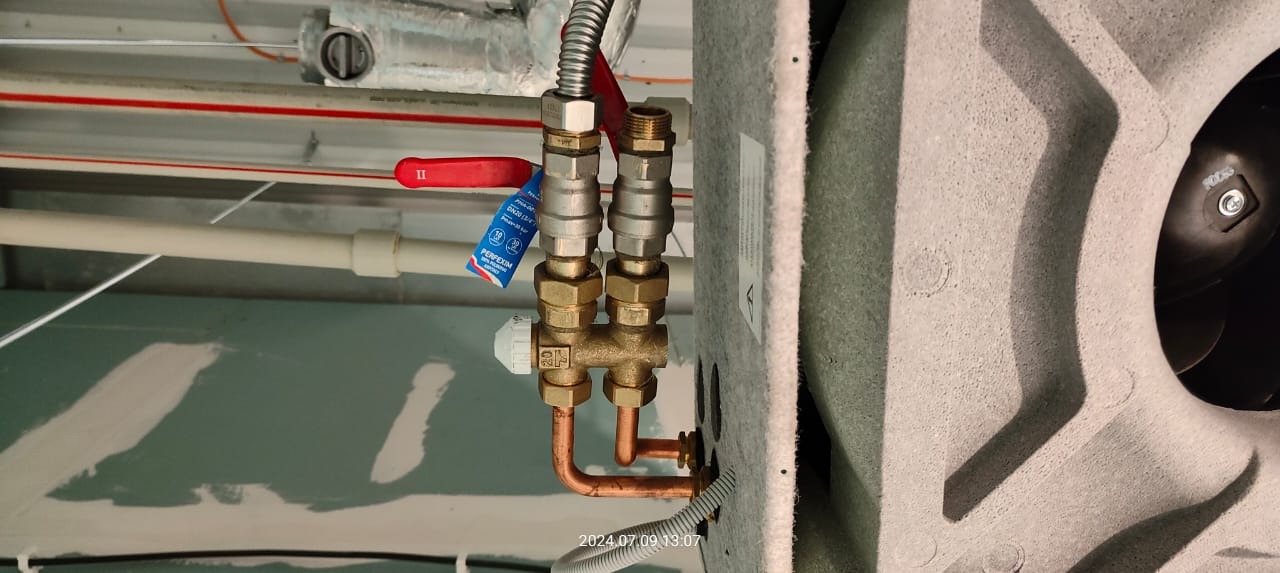 Przyłącze grzejnikowe z zaworami odcinającymi i termostatycznym, rurki miedziane, widoczna etykieta producenta zaworów, tło stanowią rury pod sufitem.