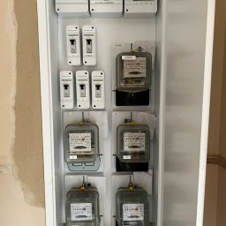 B_P ELEKTROINSTALACJE BARTOSZ PUCZKA - Szafka elektryczna z licznikami i bezpiecznikami, widoczne oznaczenia 'Blok Rozgałęźny', 'Administracja', 'Garaże', 'Klatka Piwnica', liczniki z oznaczeniem 'Admin', przewody uziemiające