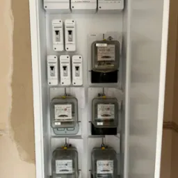 Szafka elektryczna z licznikami i bezpiecznikami, widoczne oznaczenia 'Blok Rozgałęźny', 'Administracja', 'Garaże', 'Klatka Piwnica', liczniki z oznaczeniem 'Admin', przewody uziemiające