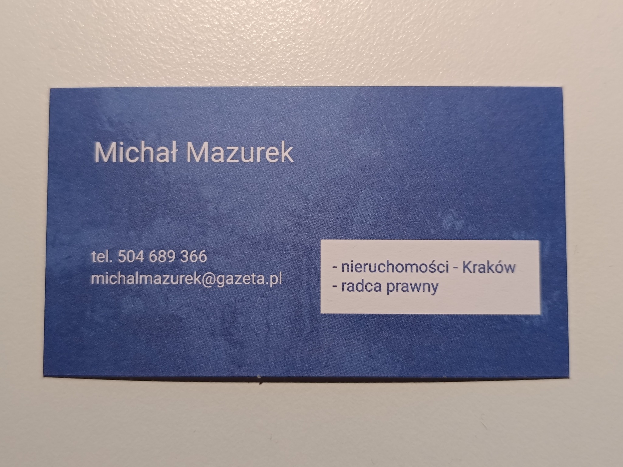 Wizytówka w odcieniach niebieskiego z danymi kontaktowymi: imię i nazwisko Michał Mazurek, numer telefonu, adres e-mail oraz informacja o specjalizacji - nieruchomości Kraków i radca prawny.