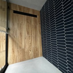 SK-Bud Sebastian Nienajadło - Nowoczesna łazienka z drewnopodobnymi płytkami i czarną ścianą z heksagonalnym wzorem. Minimalistyczny design, widoczny odpływ liniowy. Wykończenie z dbałością o detale.