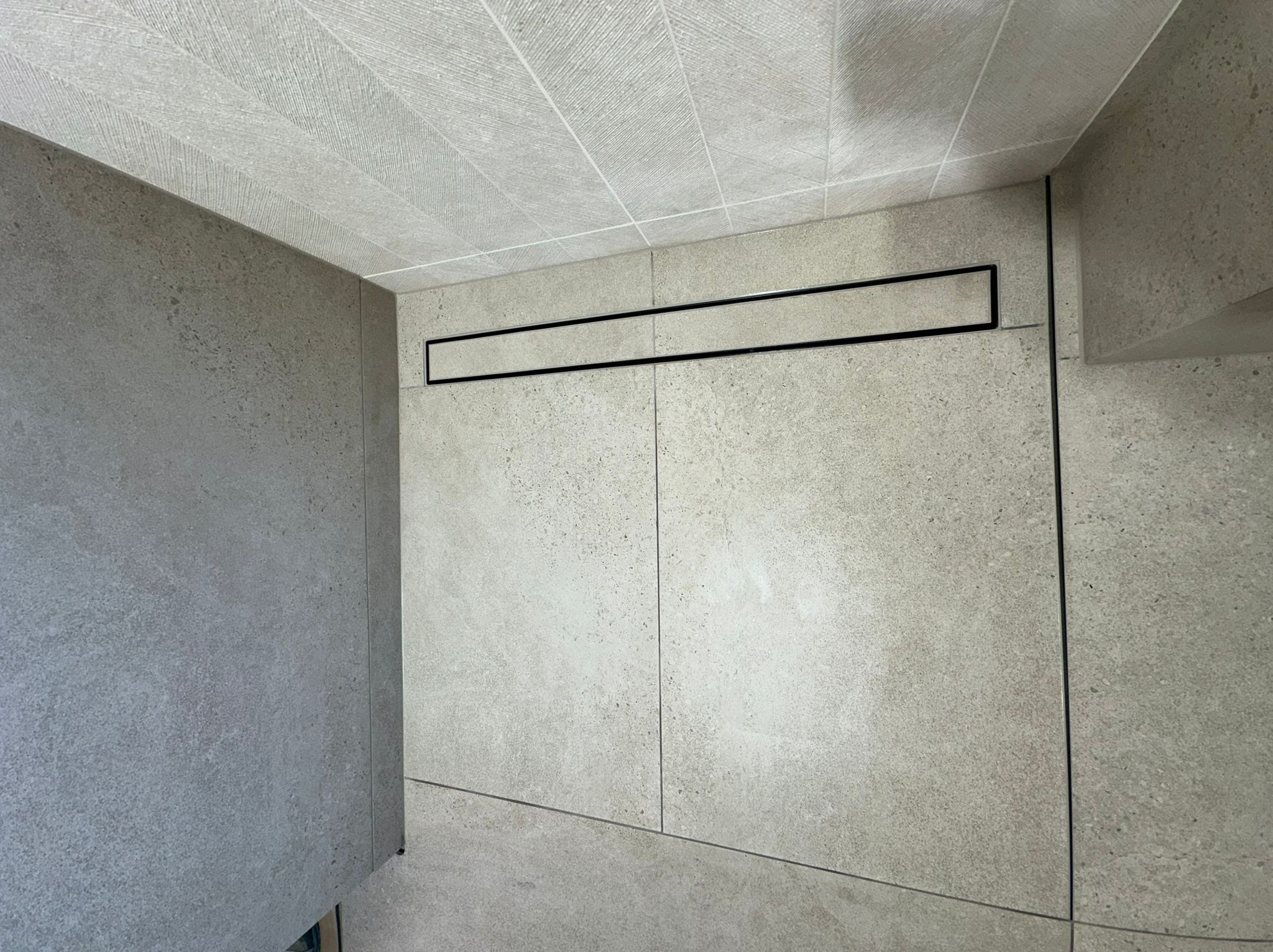 Minimalistyczna łazienka z szarymi płytkami, liniowym odpływem i wzorzystym sufitem. Nowoczesne wykończenie wnętrza.