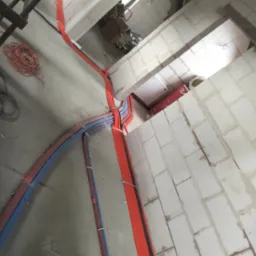 Wnętrze w trakcie prac: kable elektryczne (czerwone i niebieskie) prowadzone po ścianach z betonu komórkowego. Widoczna instalacja podtynkowa i zwój kabla.