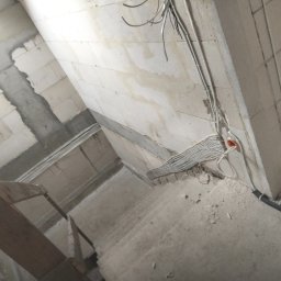 EL-KON KONRAD KUCHARCZYK - Instalacja elektryczna w surowym wnętrzu: kable ułożone wzdłuż ściany z bloczków, widoczne puszki instalacyjne i fragment rusztowania. Etap prac przed tynkowaniem.