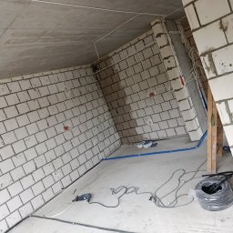 Konrad Kucharczyk - Surowy stan: wnętrze w trakcie prac, widoczne przewody elektryczne rozprowadzone po ścianach z betonu komórkowego, narzędzia i zwój kabli na podłodze.