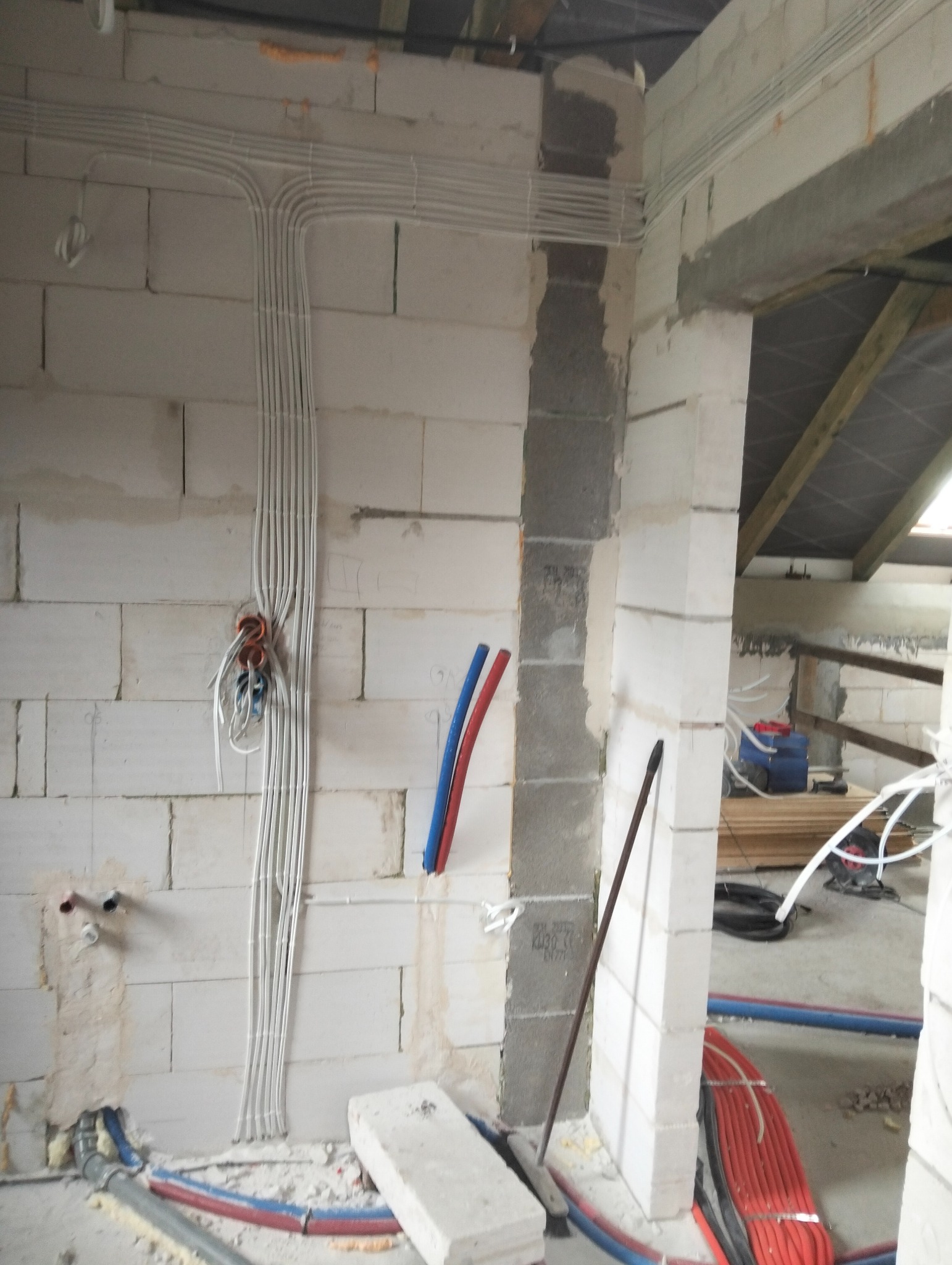 Wnętrze w trakcie prac wykończeniowych: ułożone kable elektryczne w białych rurkach na ścianie z betonu komórkowego. Widoczne także rury instalacji wodnej.