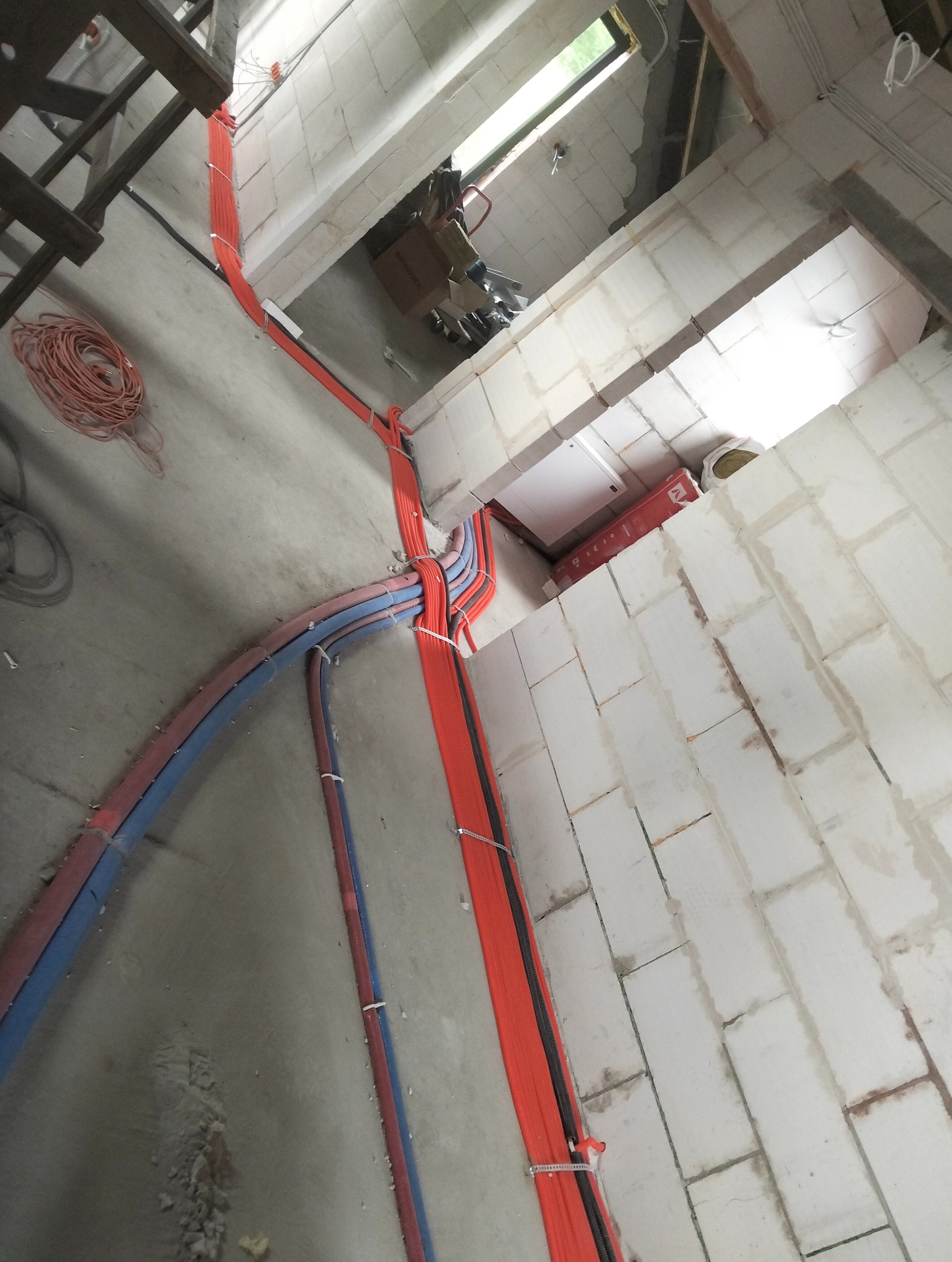 Wnętrze w trakcie prac: kable elektryczne (czerwone i niebieskie) prowadzone po ścianach z betonu komórkowego. Widoczna instalacja podtynkowa i zwój kabla.
