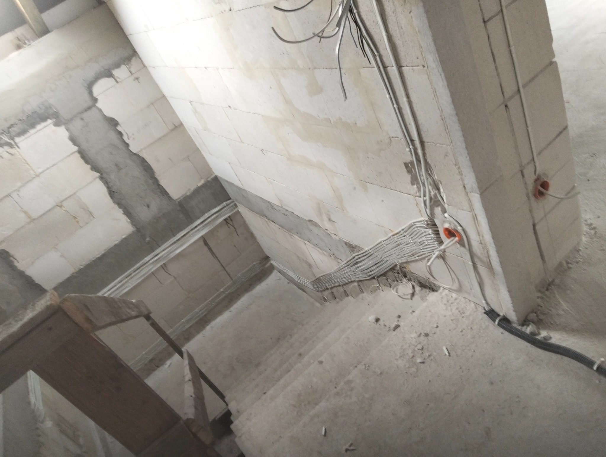 Instalacja elektryczna w surowym wnętrzu: kable ułożone wzdłuż ściany z bloczków, widoczne puszki instalacyjne i fragment rusztowania. Etap prac przed tynkowaniem.