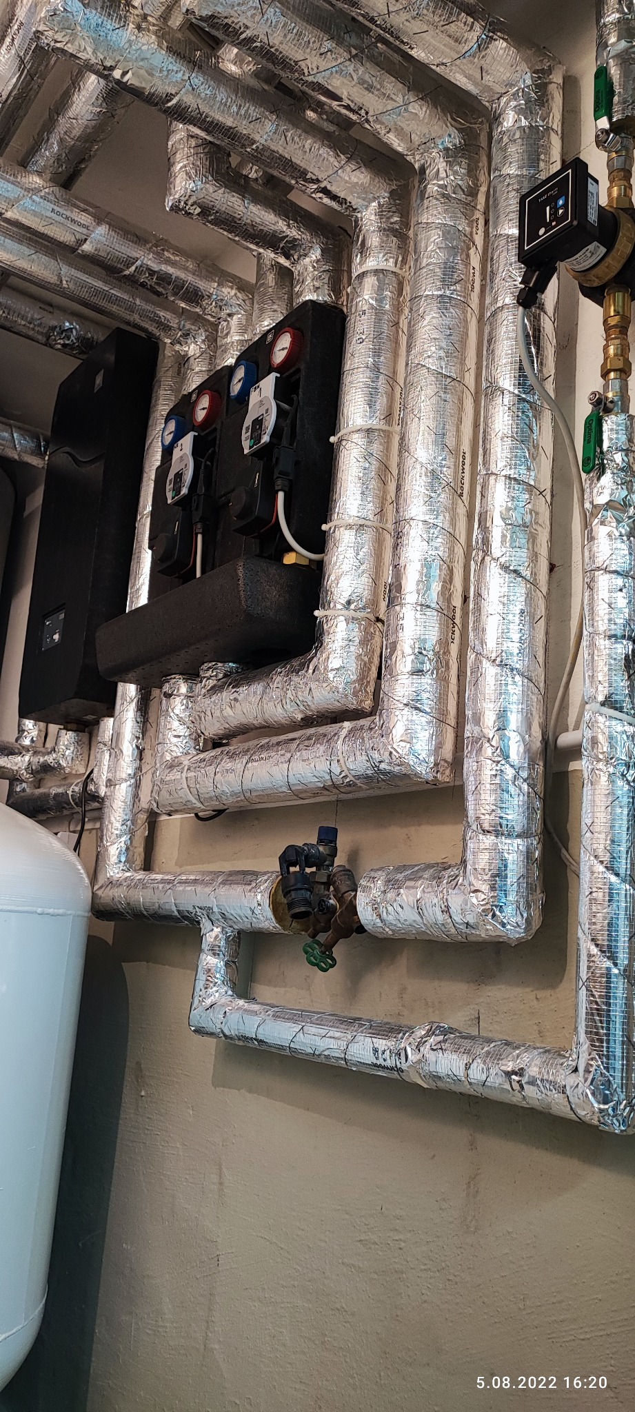 Izolowane rury instalacji grzewczej z zaworami i pompami obiegowymi w kotłowni, widoczne oznaczenia Rockwool na izolacji.