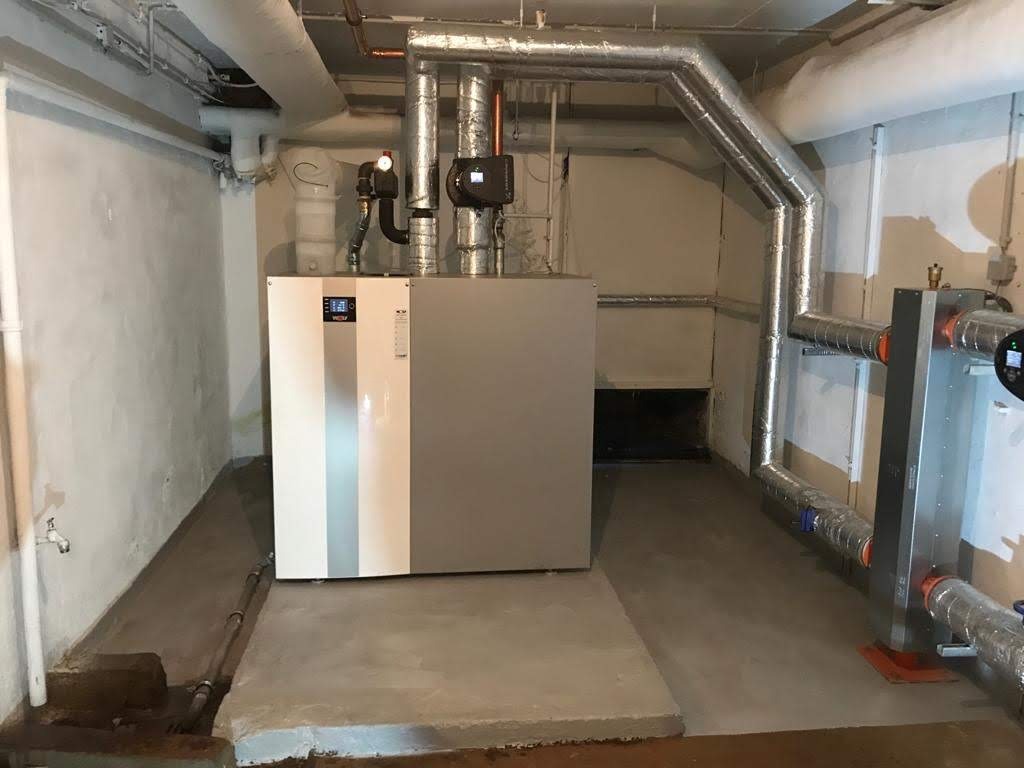 Nowoczesny piec grzewczy z szarym panelem, rurami izolowanymi termicznie i automatyką w piwnicy z surowymi ścianami.