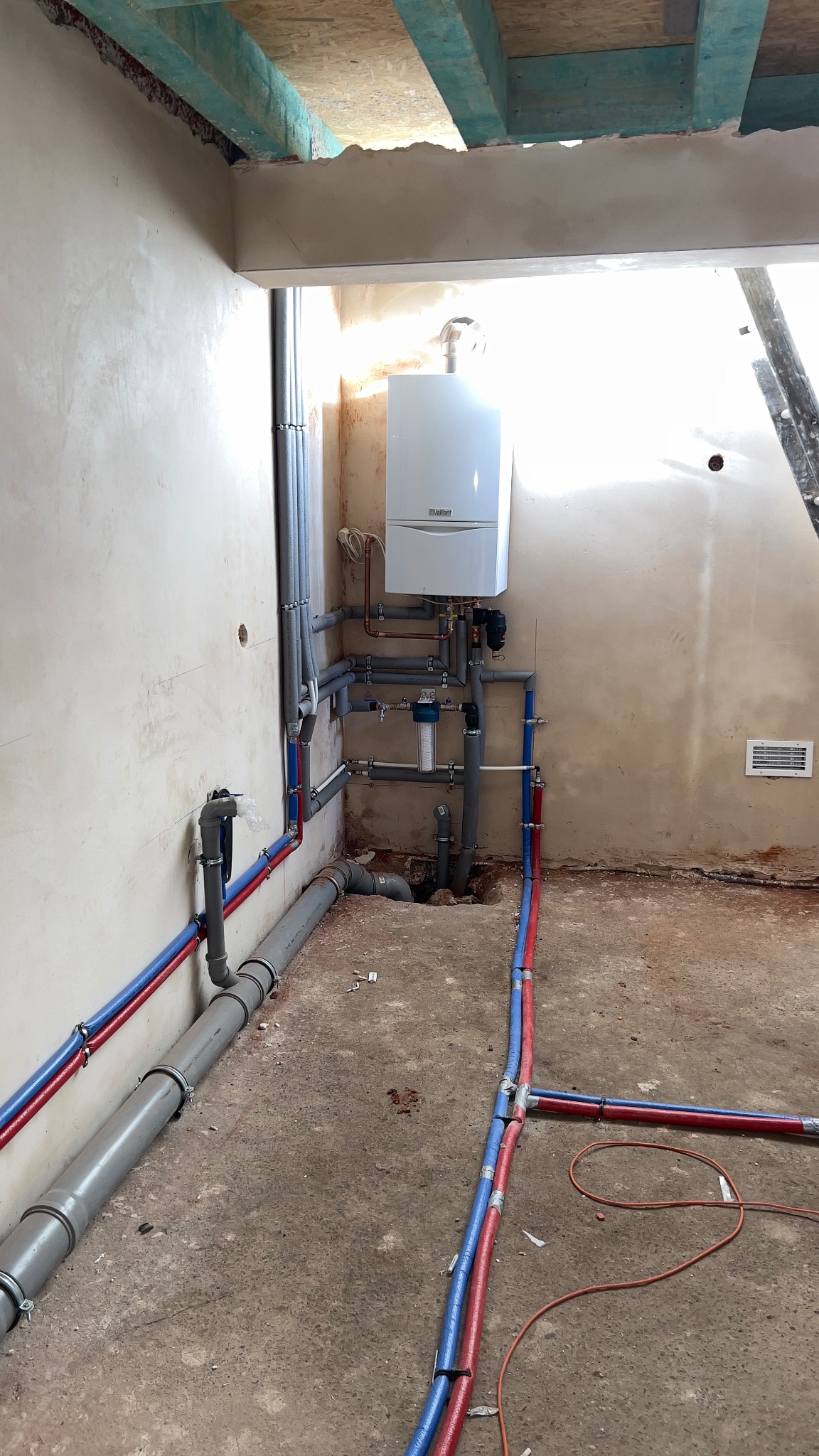 Instalacja CO z piecem gazowym Vaillant i filtrem wody, rury PEX w izolacji czerwono-niebieskiej. Realizacja w Rybnicy. Szare rury kanalizacyjne.