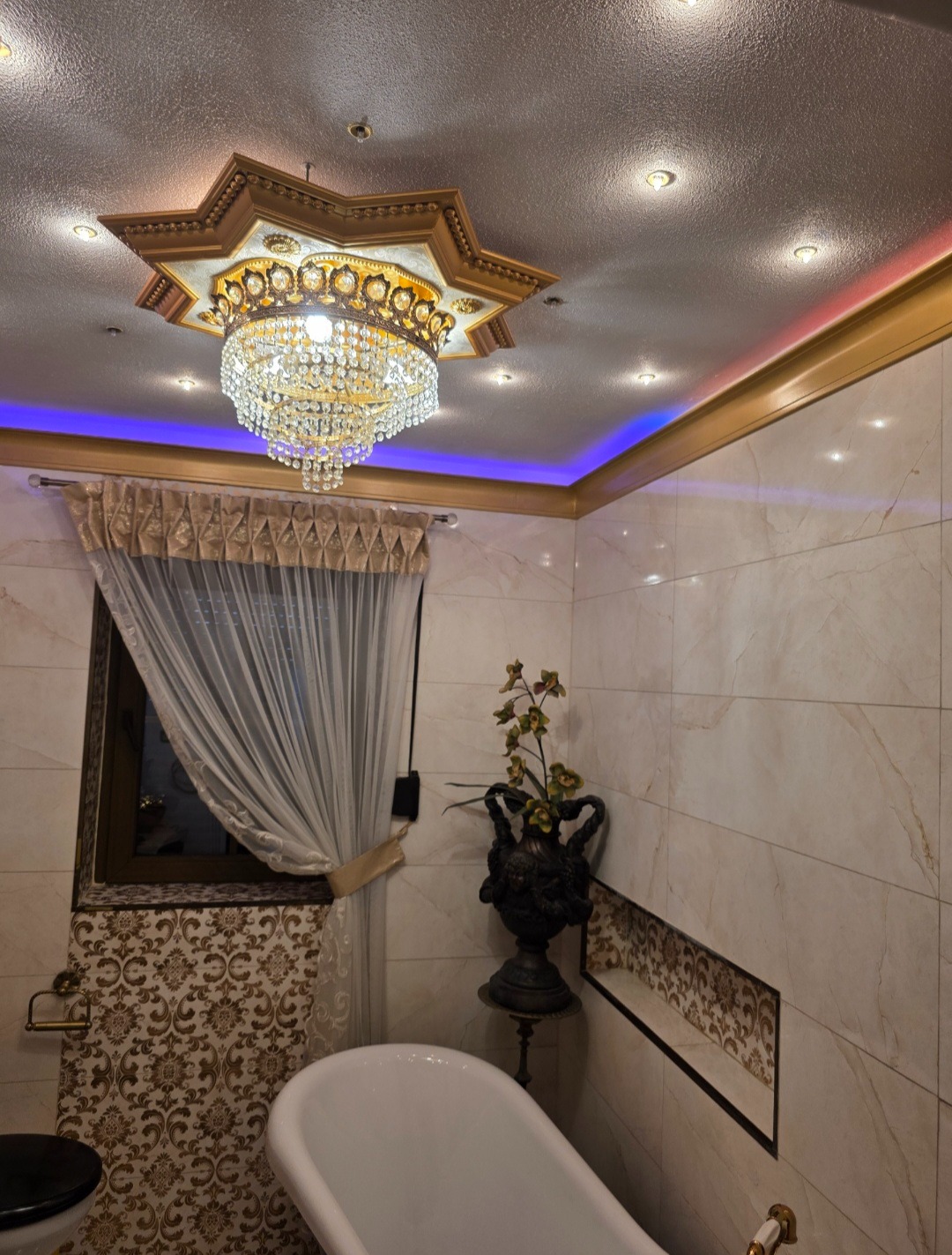 Luksusowa łazienka z marmurowymi płytkami, wolnostojącą wanną i kryształowym żyrandolem w stylu glamour, oświetlona niebieskimi neonami.