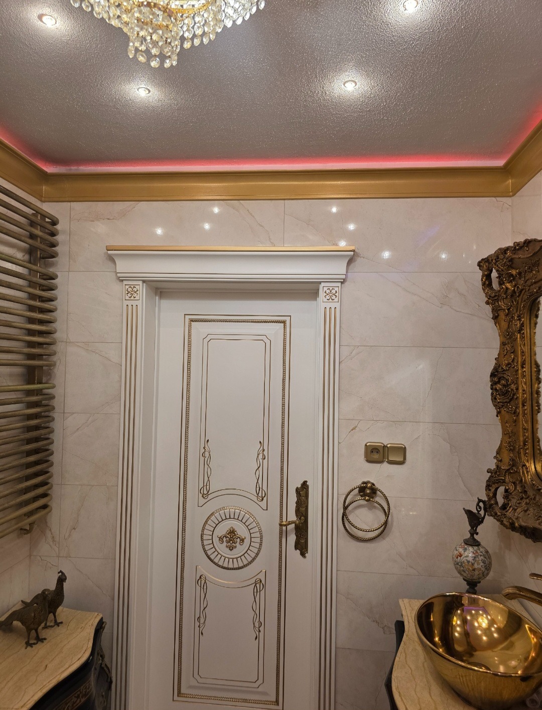 Ekskluzywna łazienka w stylu glamour: białe marmurowe płytki, złote akcenty, ozdobne lustro i kryształowy żyrandol. Luksusowe wykończenie wnętrza.