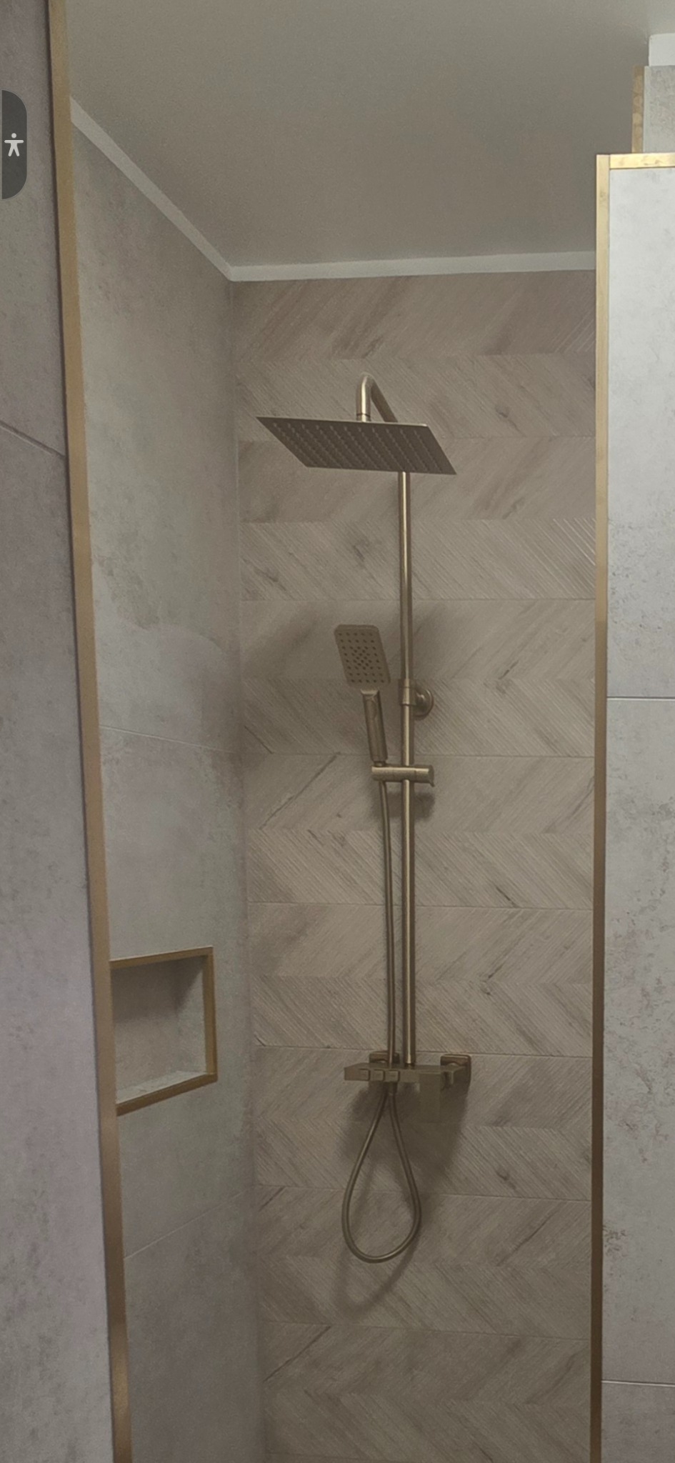 Nowoczesna kabina prysznicowa z deszczownicą w odcieniach beżu i złota. Ściany wyłożone płytkami imitującymi drewno ułożone w jodełkę. Minimalistyczny design.