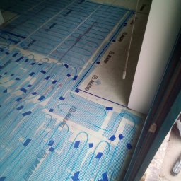 K.m.r - Rozłożona mata grzewcza podłogowa Mapei, przygotowana do wylewki, widok z góry, fragment okna w prawym dolnym rogu.