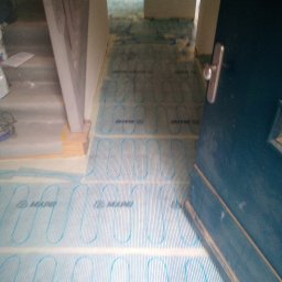 K.m.r - Rozłożona mata grzewcza Mapei na podłodze w trakcie prac przygotowawczych do wykończenia podłogi, widoczny próg drzwi i fragment ściany.