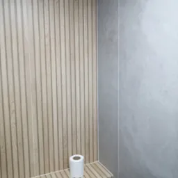 Nowoczesna łazienka z drewnopodobnymi panelami ściennymi i szarymi płytkami, rolka papieru toaletowego na półce.