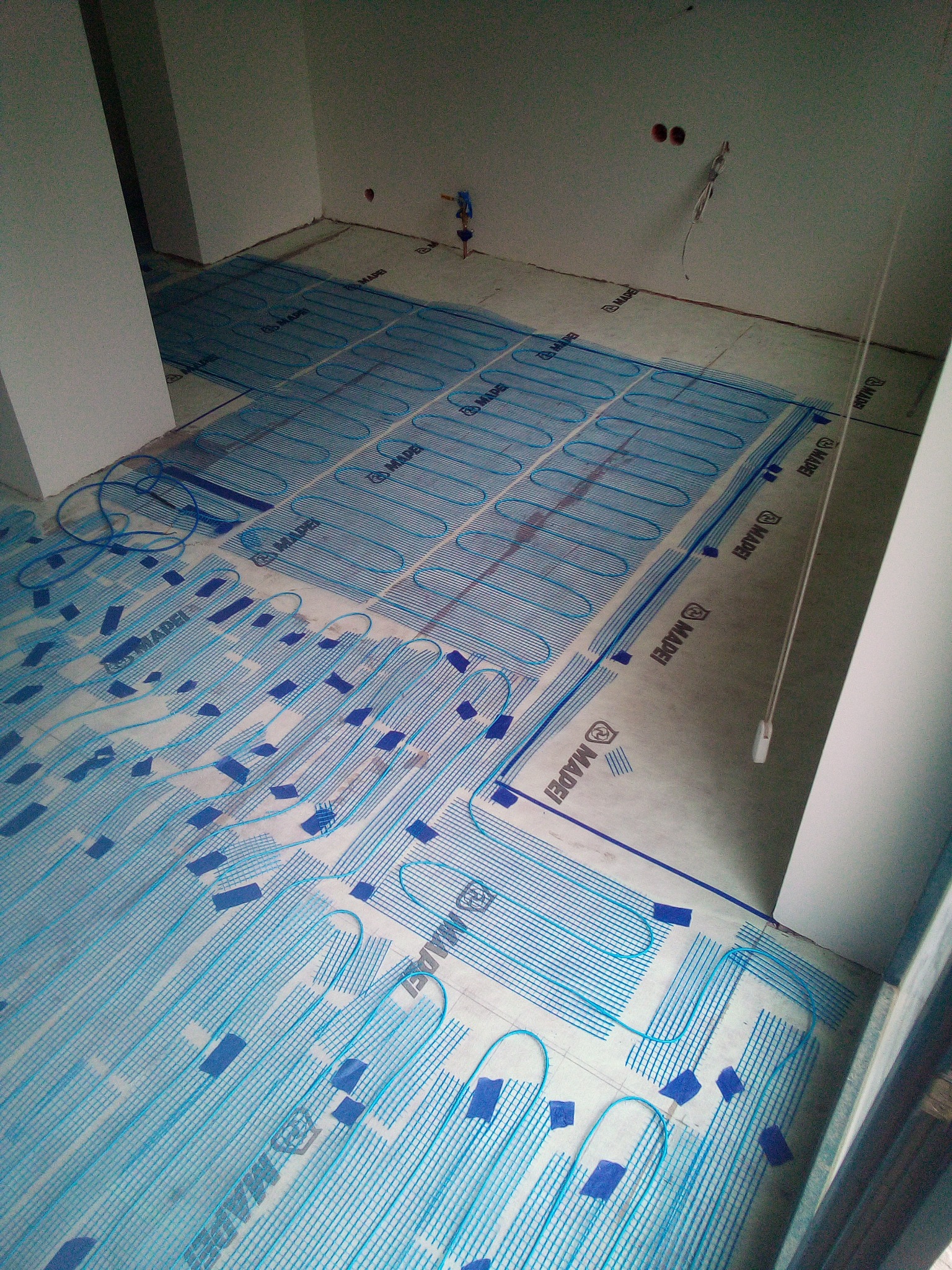 Rozłożona mata grzewcza podłogowa Mapei, zabezpieczona niebieską taśmą, w surowym stanie, przygotowana do wylewki w remontowanej łazience.