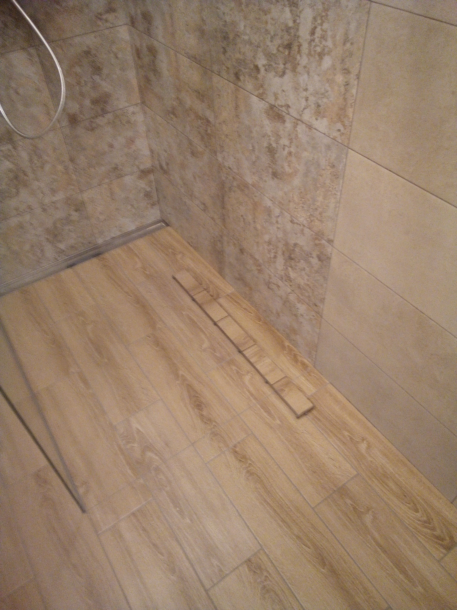 Układanie podłogi z płytek imitujących drewno w łazience, widoczne niedokończone fragmenty przy ścianie z beżowych płytek.