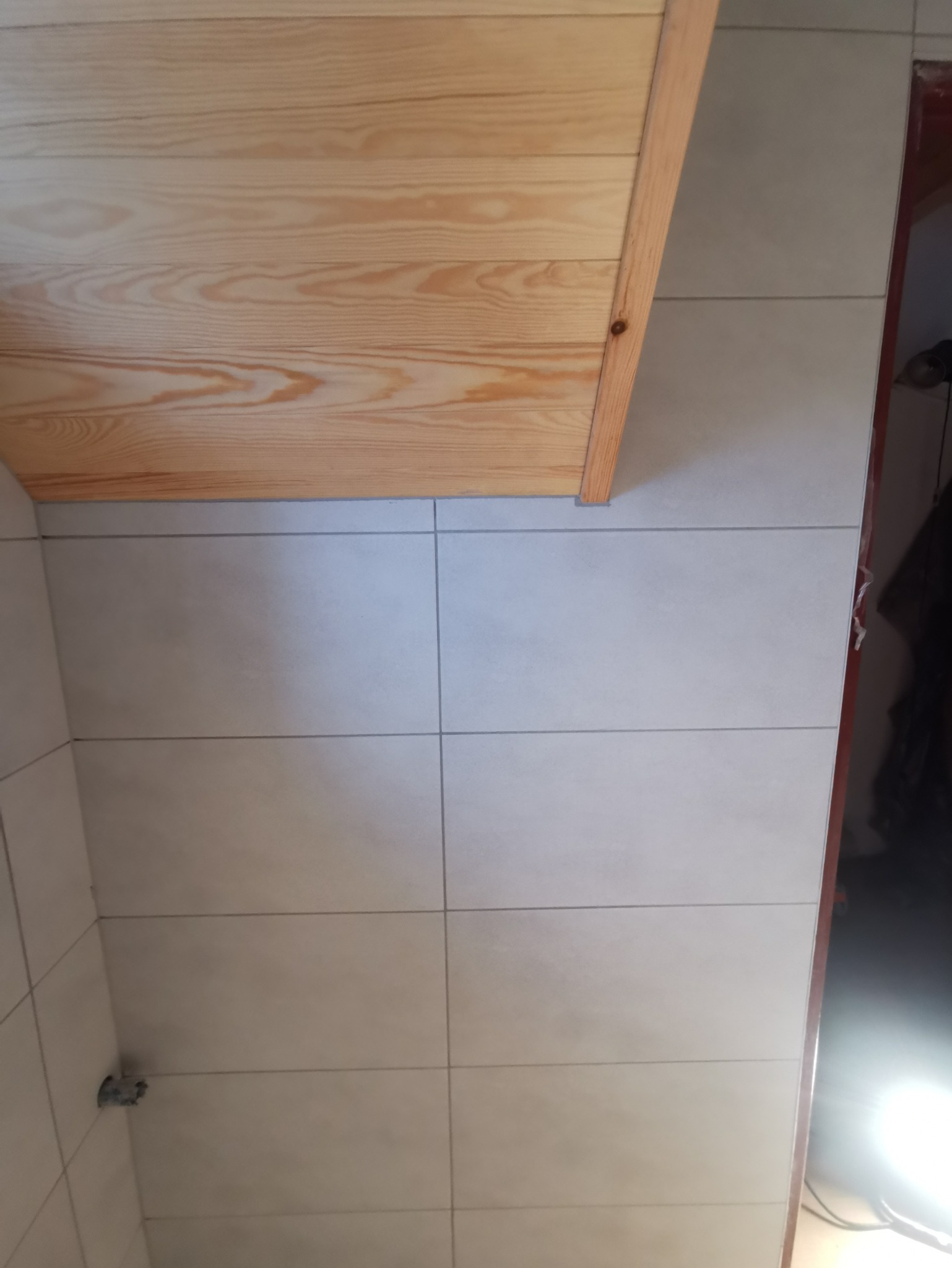 Ściana w łazience wyłożona jasnymi, prostokątnymi płytkami ceramicznymi z wąskimi fugami, widoczna drewniana obudowa sufitu z boazerii.