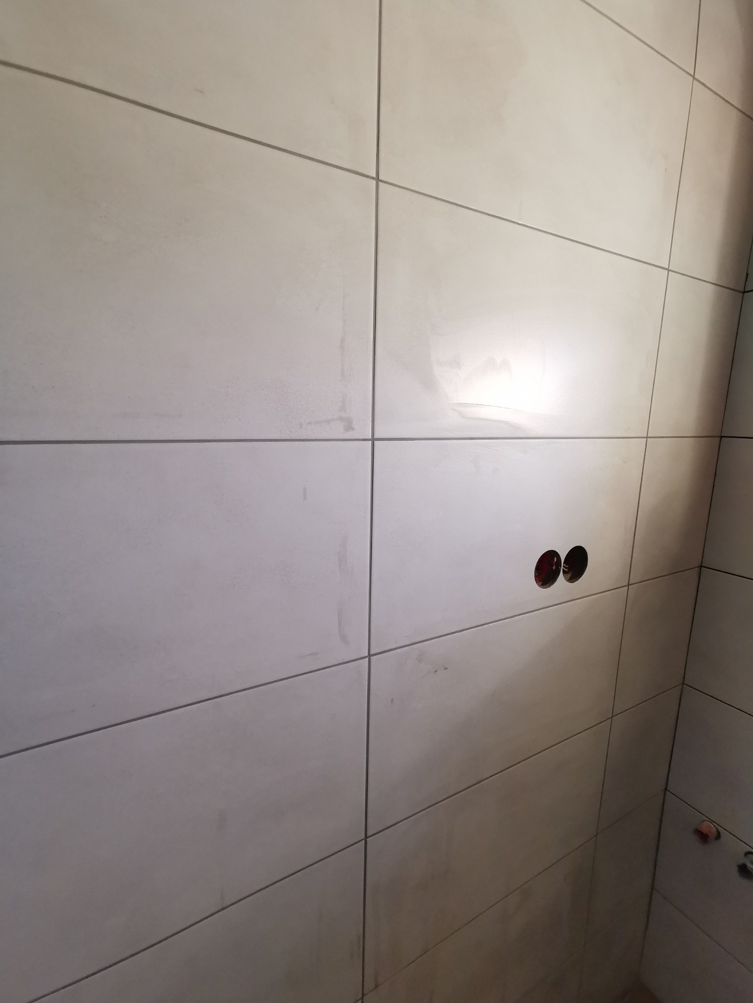 Ściana wyłożona beżowymi, matowymi płytkami ceramicznymi z widocznymi otworami na gniazdka elektryczne, w trakcie prac wykończeniowych.